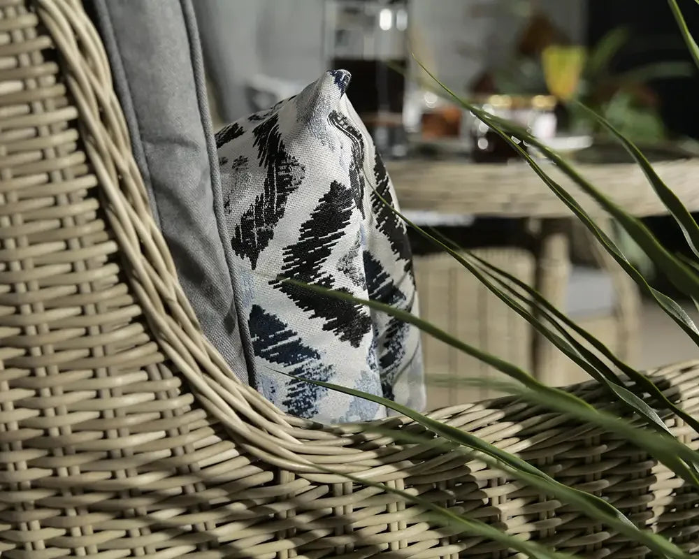 Close view of wicker dining chair with grey cushion and patterned pillow