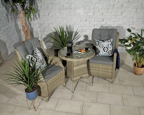 Rattan bistro set with two grey cushioned chairs and glass table in a modern indoor setting