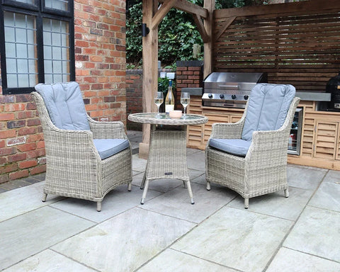 Rattan garden bistro set with two cushioned armchairs and round table on patio