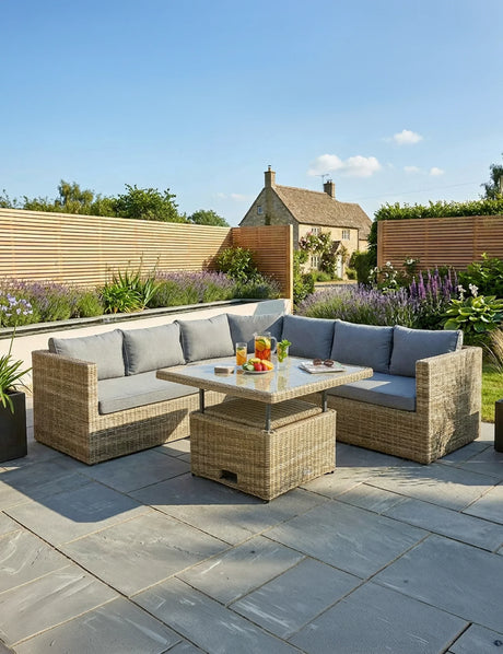 Rattan garden corner sofa set with grey cushions and glass top table on stone patio