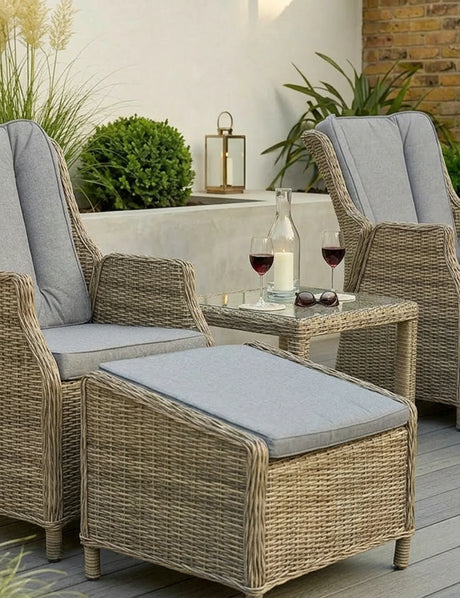 Rattan garden lounge set with two chairs, ottoman, side table, and grey cushions on patio