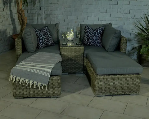 Rattan corner sofa set with grey cushions, striped throw, and glass top table on patio
