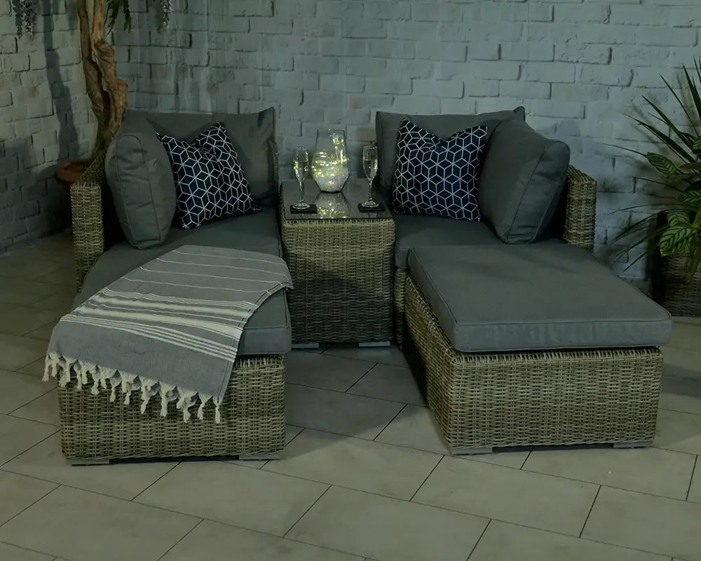 Rattan corner sofa set with grey cushions, striped throw, and glass top table on patio