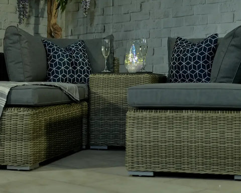 Rattan garden furniture set with grey cushions, patterned pillows and glass tabletop