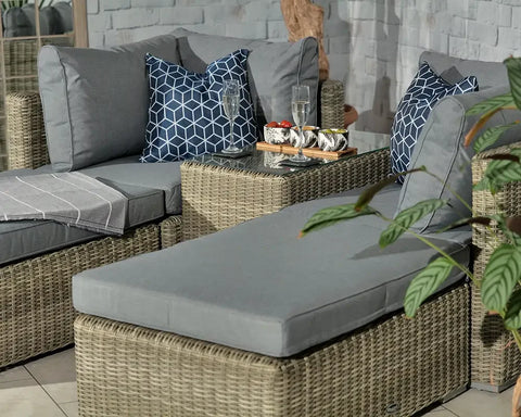 Grey rattan corner sofa set with cushions and glass top table in indoor lounge area