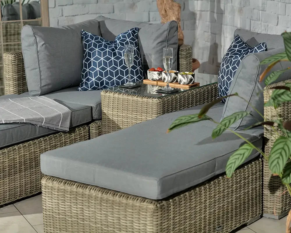 Grey rattan corner sofa set with cushions and glass top table in indoor lounge area