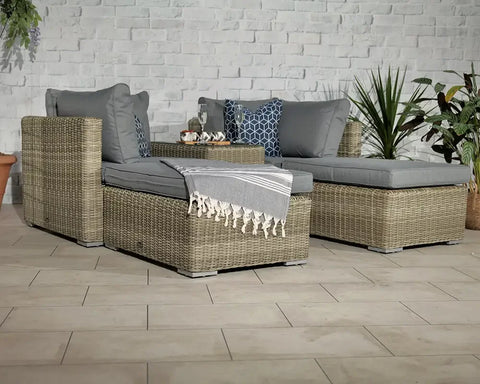 Grey rattan garden sofa set with cushions, throw, and coffee table on tiled patio