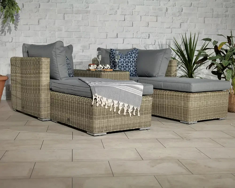 Grey rattan garden sofa set with cushions, throw, and coffee table on tiled patio