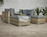 Grey rattan garden sofa set with cushions, throw, and coffee table on tiled patio