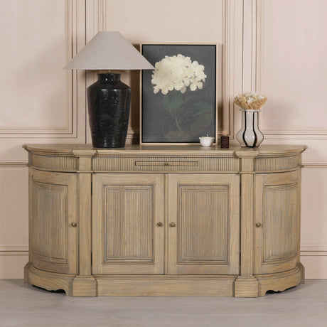 Rustic wooden buffet sideboard with fluted detailing, styled with a lamp, vase, and framed artwork against a neutral wall.