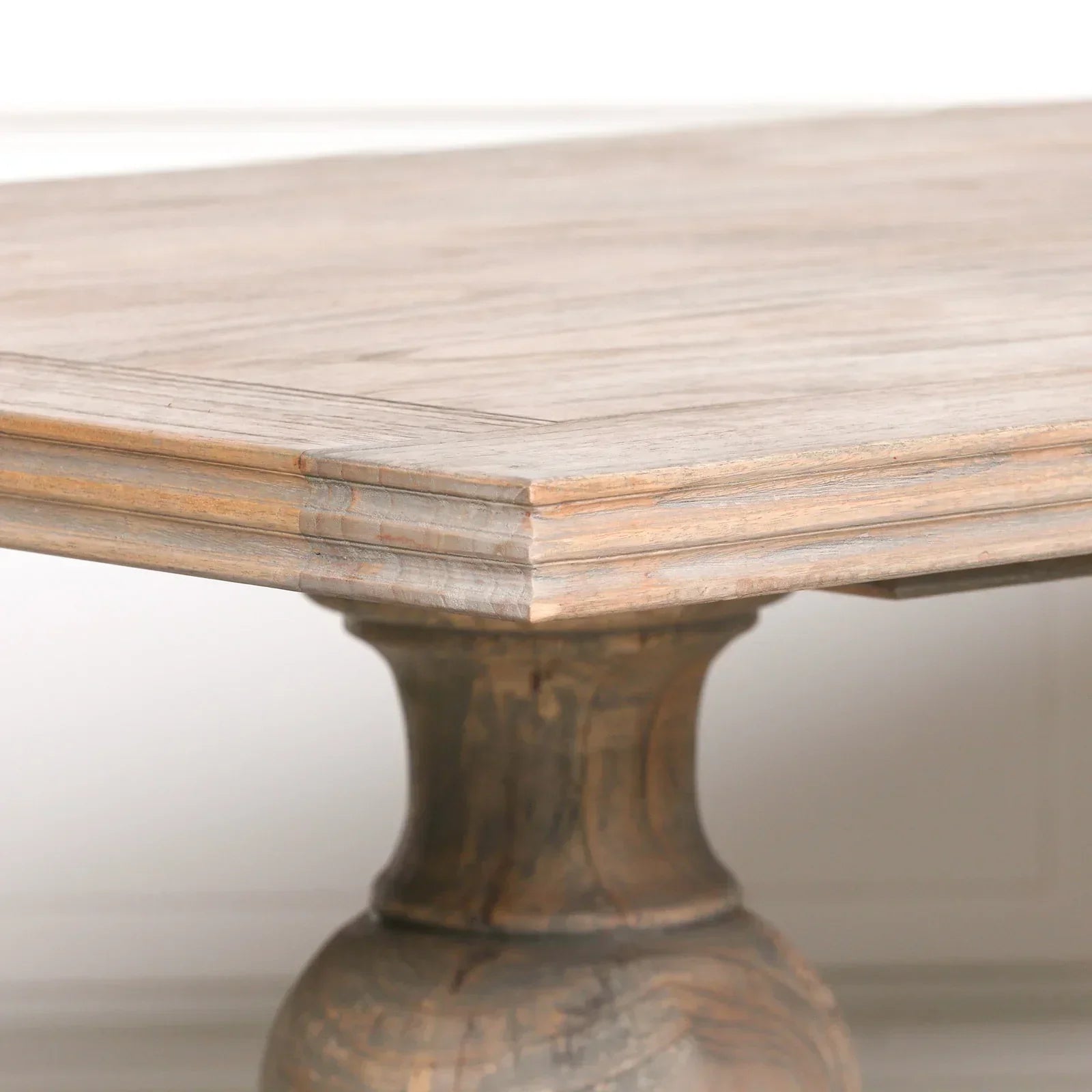 Close up of wooden dining table corner with carved pedestal leg and natural finish