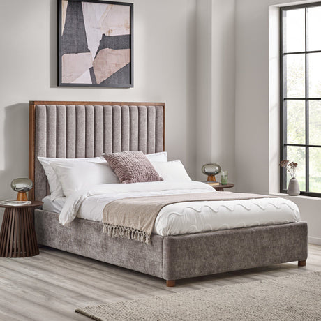 Upholstered bed in grey fabric with tall channel-tufted headboard framed in dark wood, bedding and nightstands