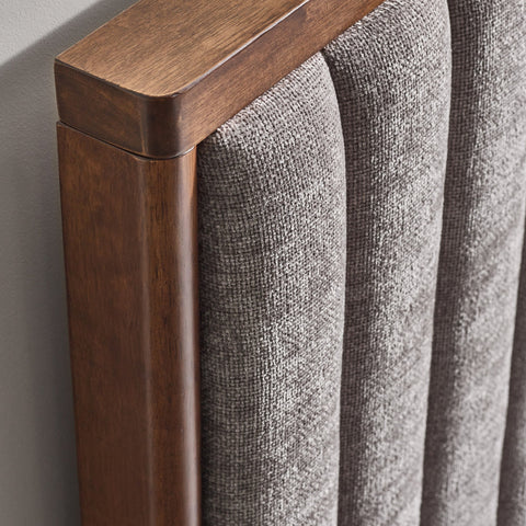 Close-up of the texture and fabric of grey upholstered bed frame and part of wooden leg