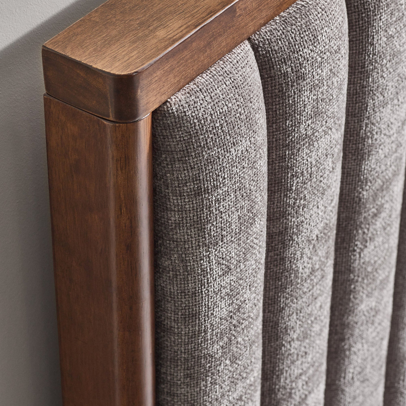 Close-up of the texture and fabric of grey upholstered bed frame and part of wooden leg