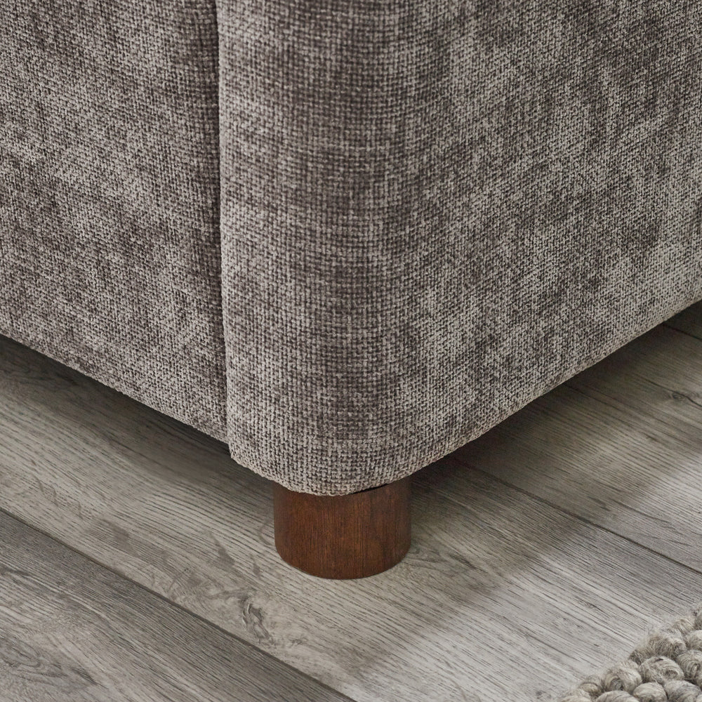 Close-up corner view of rounded wooden bed leg against wood floor and grey upholstery