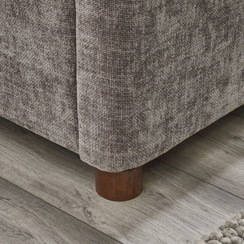 Close-up corner view of rounded wooden bed leg against wood floor and grey upholstery
