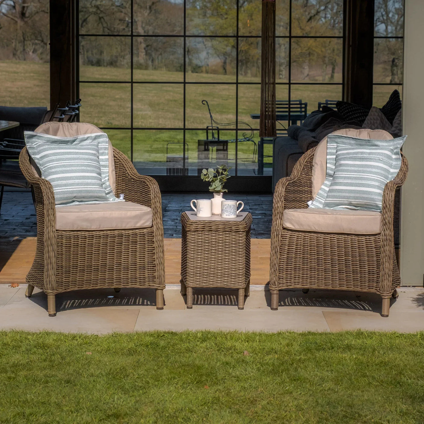 Rattan garden bistro set with two cushioned chairs and a matching side table on patio