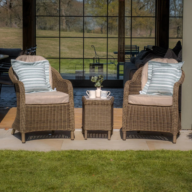 Rattan garden bistro set with two cushioned chairs and a matching side table on patio