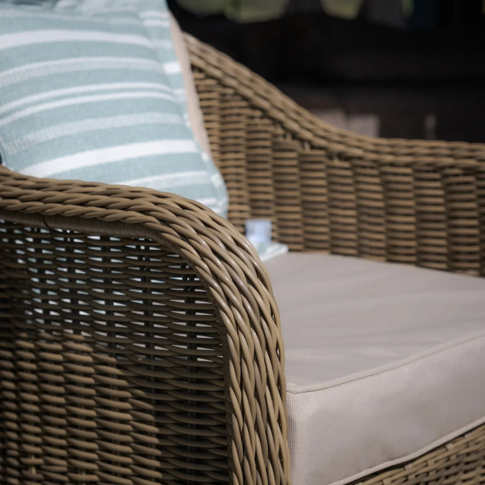 Tan rattan outdoor armchair with beige cushion and striped pillow