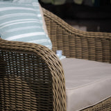 Tan rattan outdoor armchair with beige cushion and striped pillow
