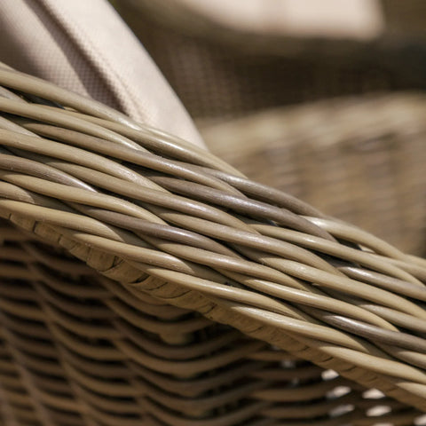 Closeup of woven rattan garden furniture arm with beige cushion fabric detail