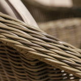 Closeup of woven rattan garden furniture arm with beige cushion fabric detail