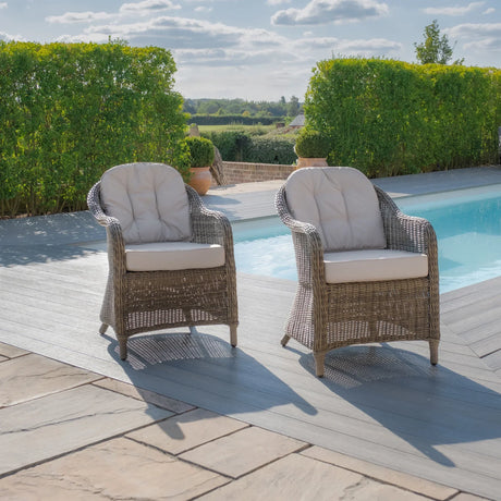 Rattan garden armchairs with cream cushions beside a pool on a patio