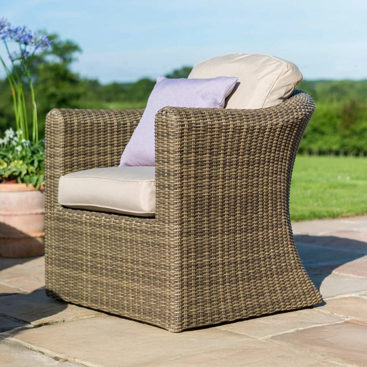 Brown rattan outdoor armchair with beige cushion and lilac pillow on patio