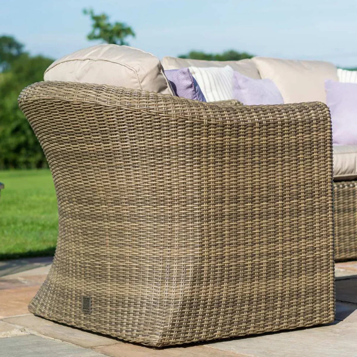 Curved rattan garden sofa with beige cushions and pillows on patio