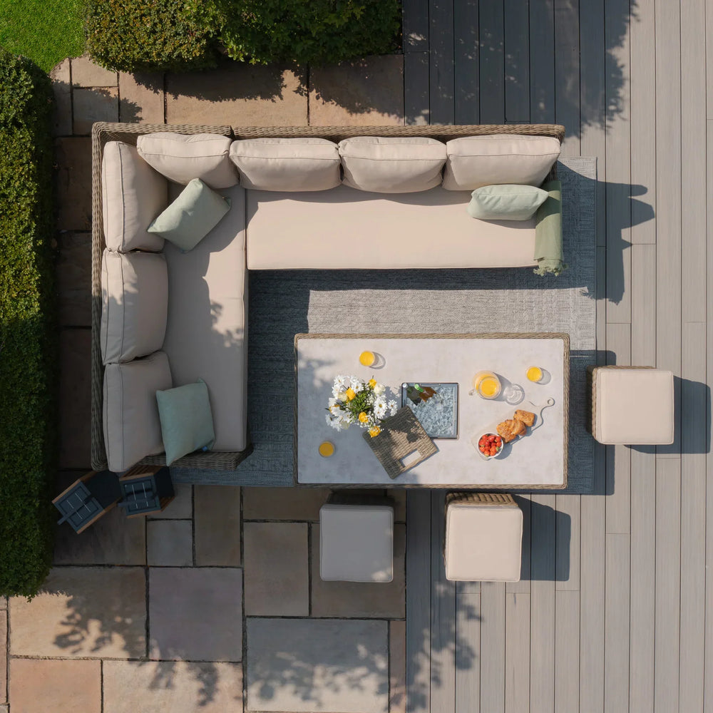 Rattan corner garden sofa set with cream cushions, dining table and stools on patio