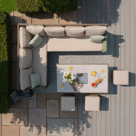 Rattan corner garden sofa set with cream cushions, dining table and stools on patio