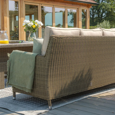 Rattan outdoor sofa with beige cushions and green throw on patio decking
