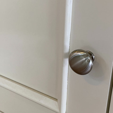 Metallic cabinet knob on a white cabinet door