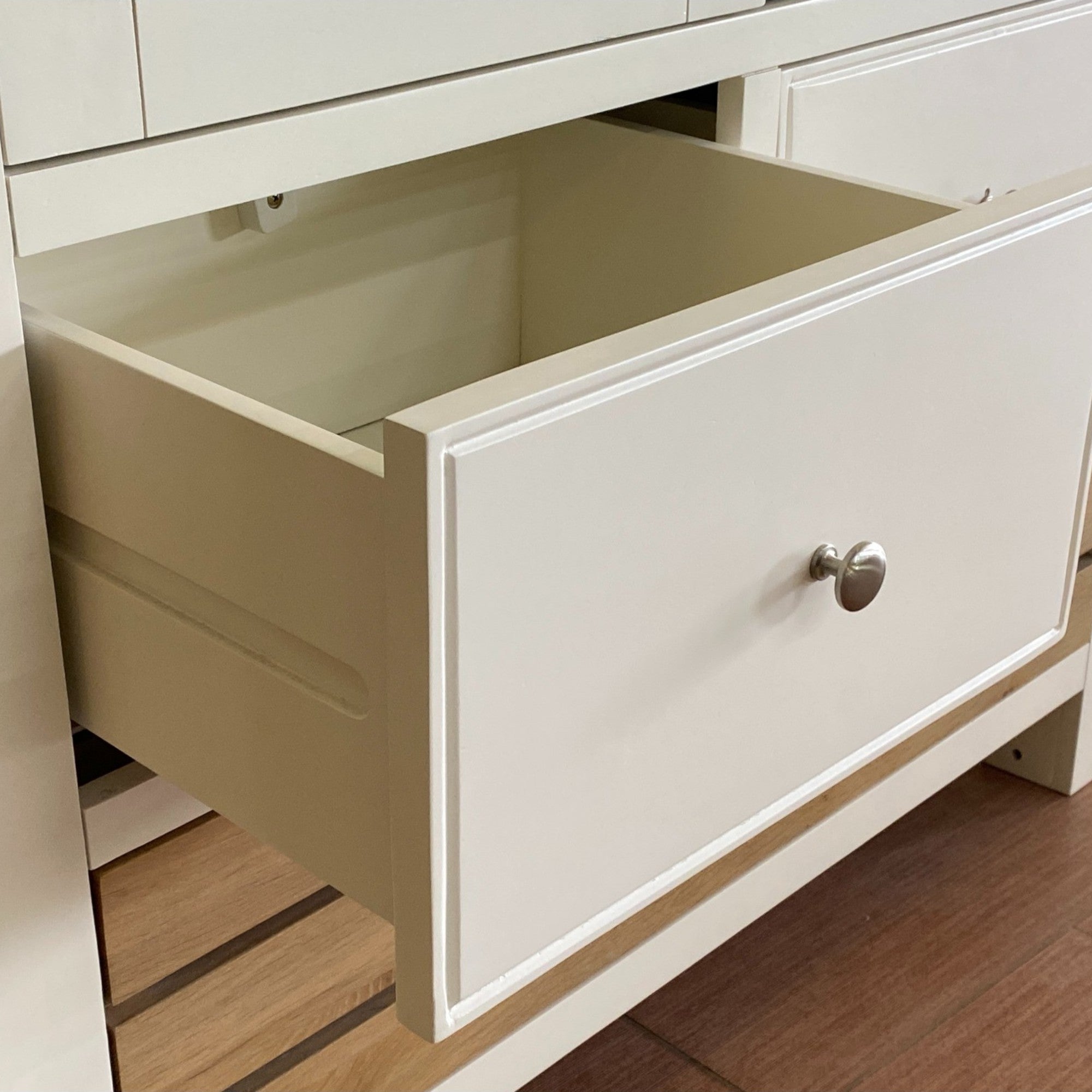 Open drawer of a white cabinet with a visible knob on a wooden floor.