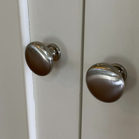 Two silver cabinet knobs on a white cabinet door.