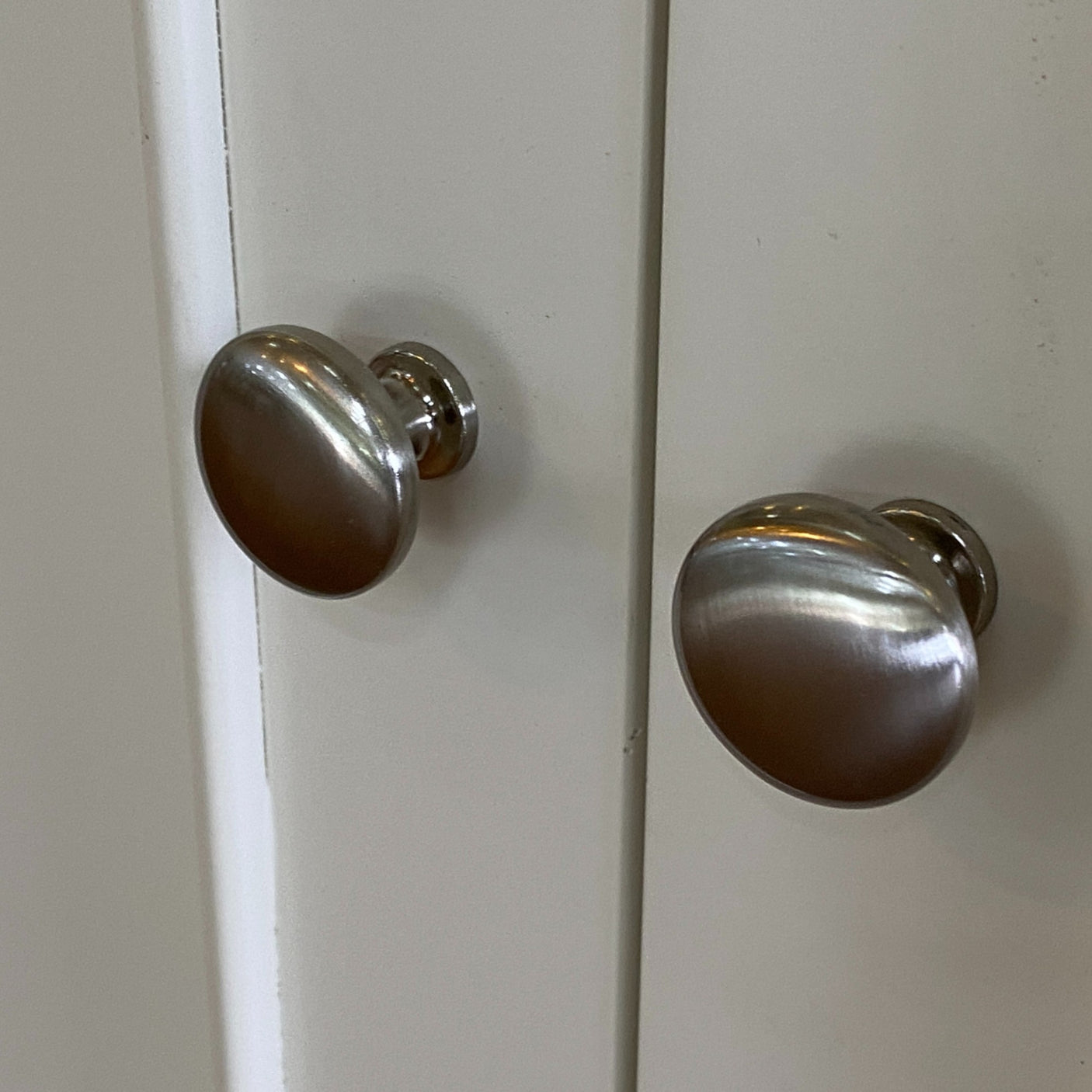 Two silver cabinet knobs on a white cabinet door.