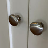 Two silver cabinet knobs on a white cabinet door.