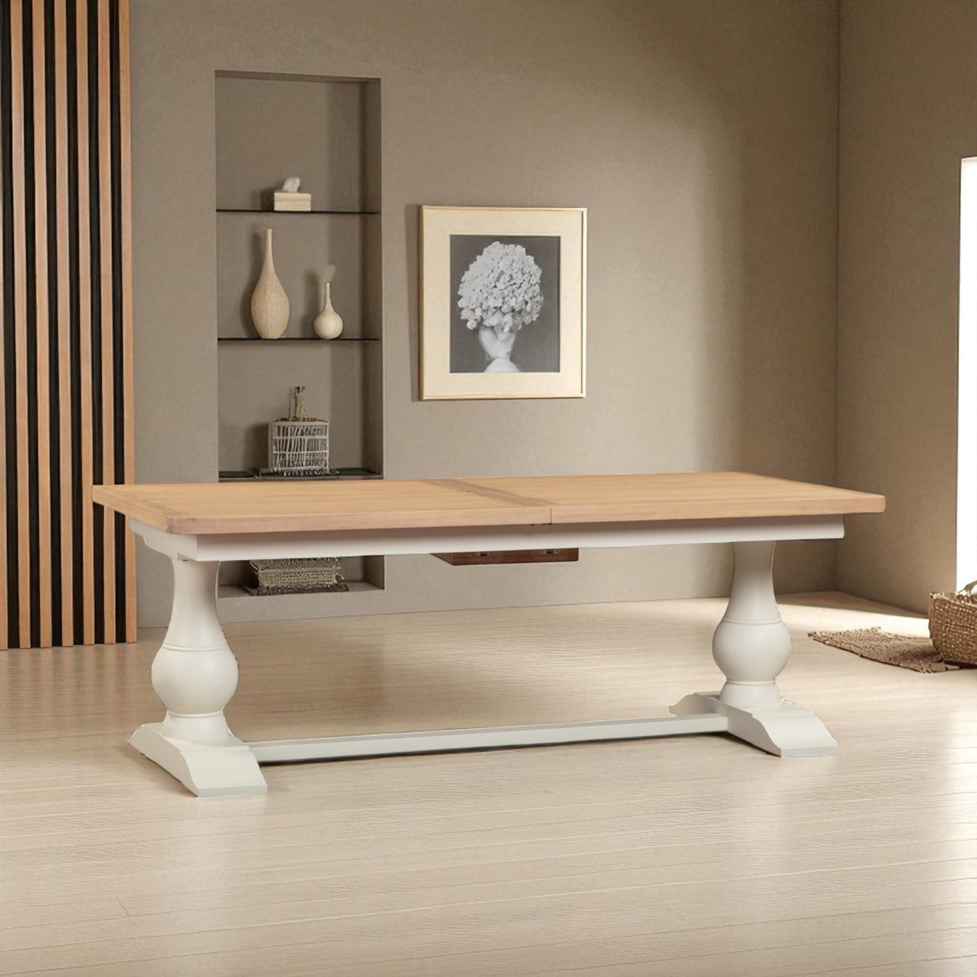 Wooden dining table with white base in a room with shelves and a painting on the wall.