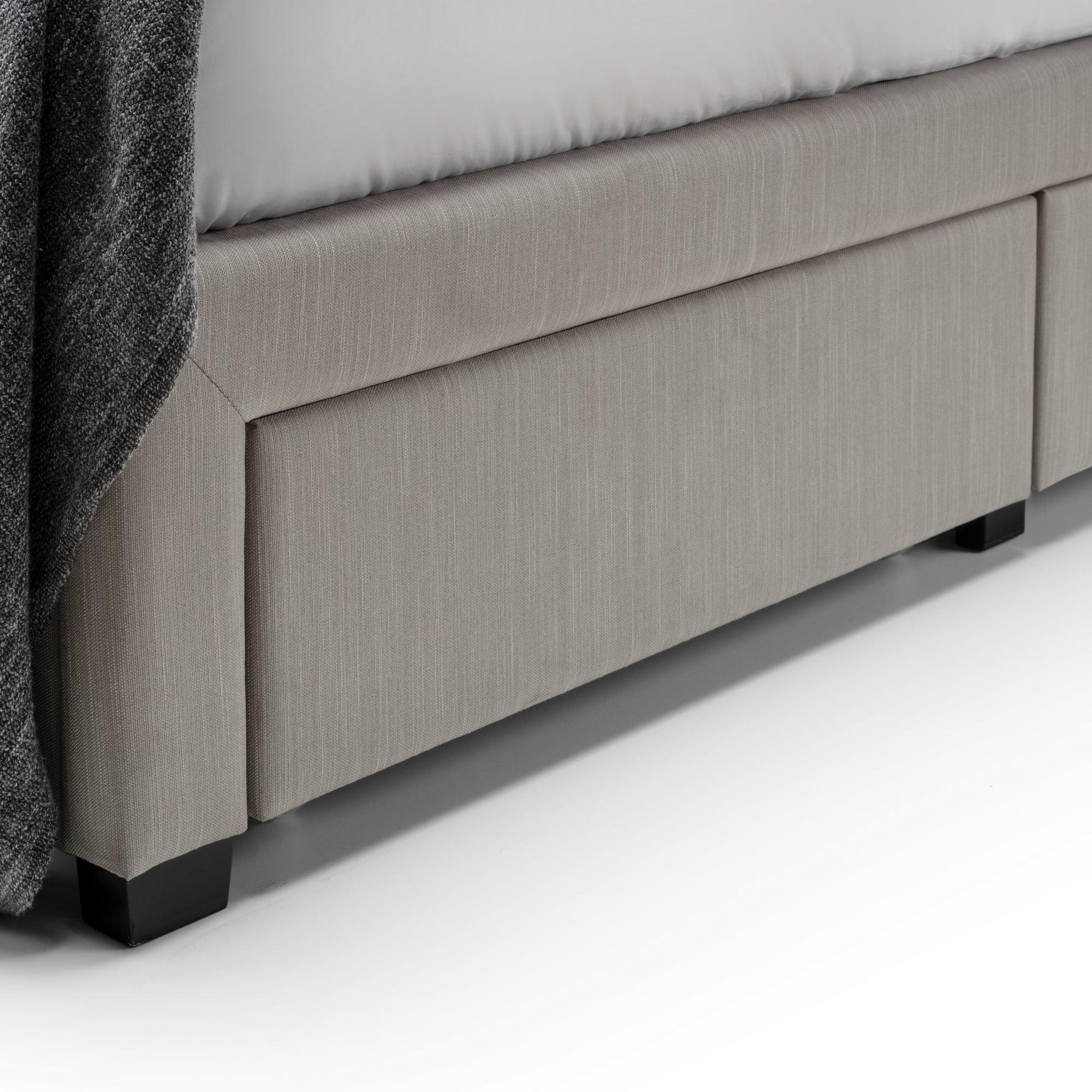 Grey upholstered bed frame with integrated storage drawer and dark wooden legs