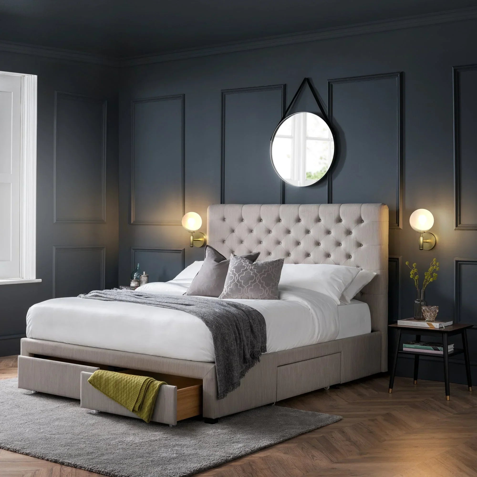 Beige upholstered storage bed with tufted headboard, open drawers, side table, and grey walls