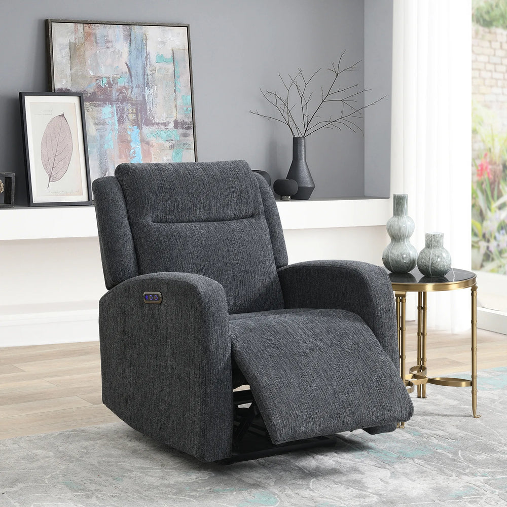 A dark gray upholstered recliner chair shown in a styled living room setting with a side table, framed wall art, and a window.