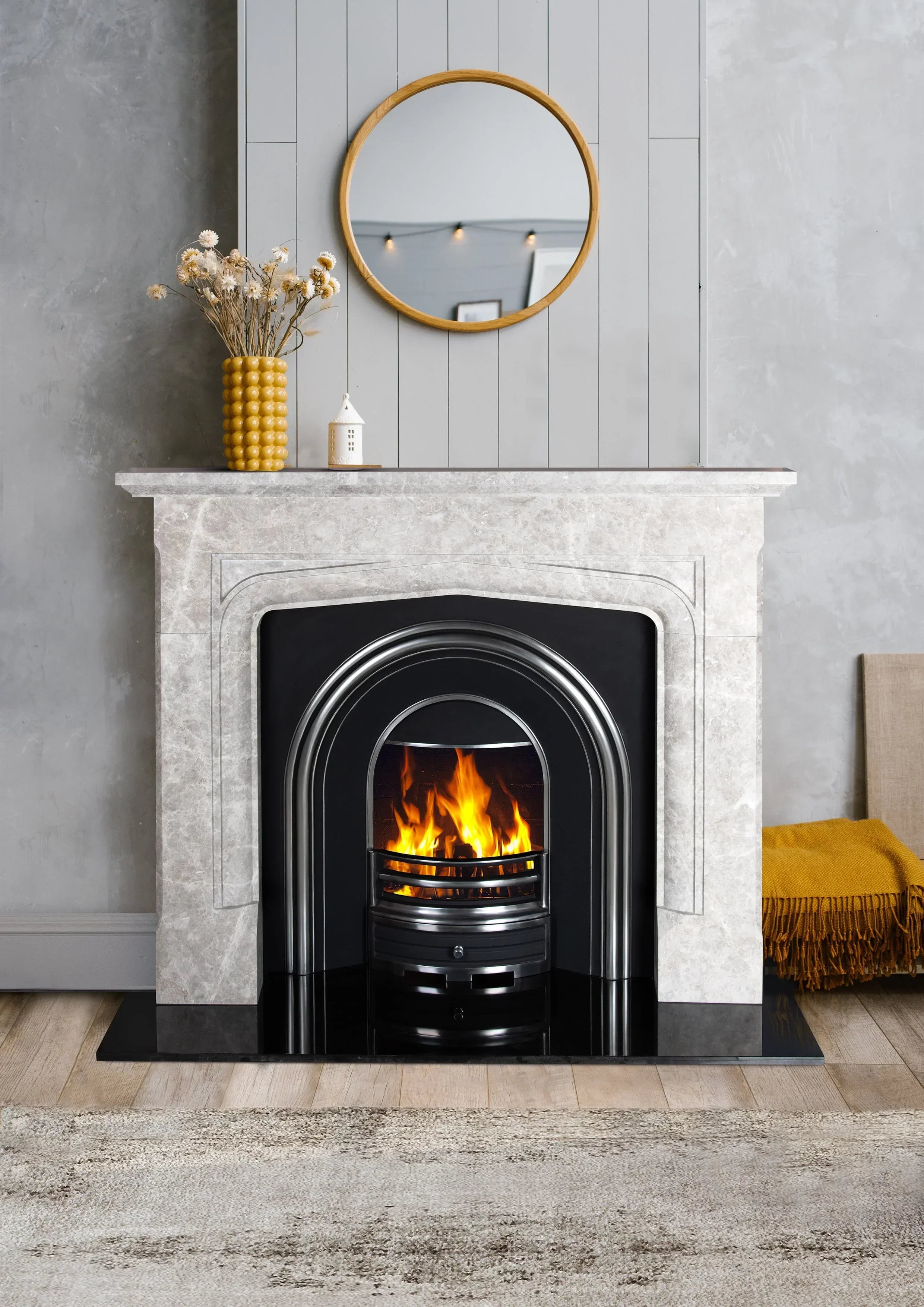Grey marble fireplace with fire grate, round wall mirror, and yellow vase on mantel