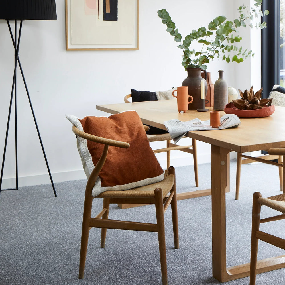 Oak dining table with modern wooden chairs, burnt orange cushion, ceramic vases and greenery