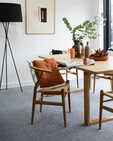 Oak dining table with modern wooden chairs, burnt orange cushion, ceramic vases and greenery