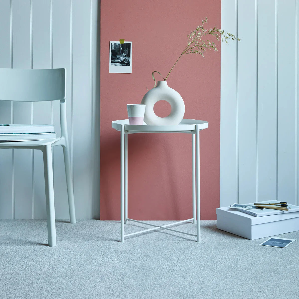 Round white side table with open vase and cup beside modern chair on carpeted floor