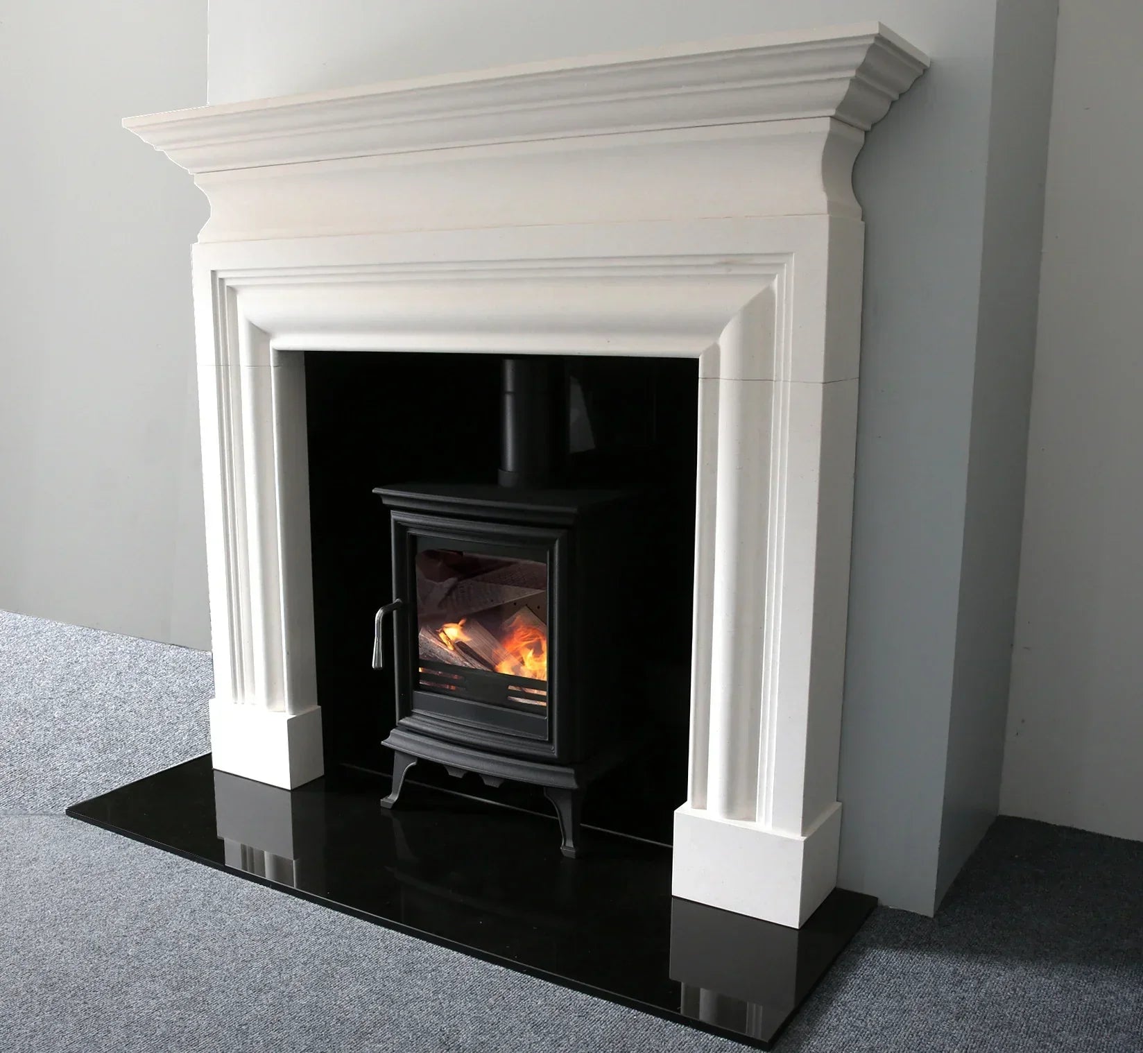 White limestone fireplace with black wood burning stove and live fire on black hearth