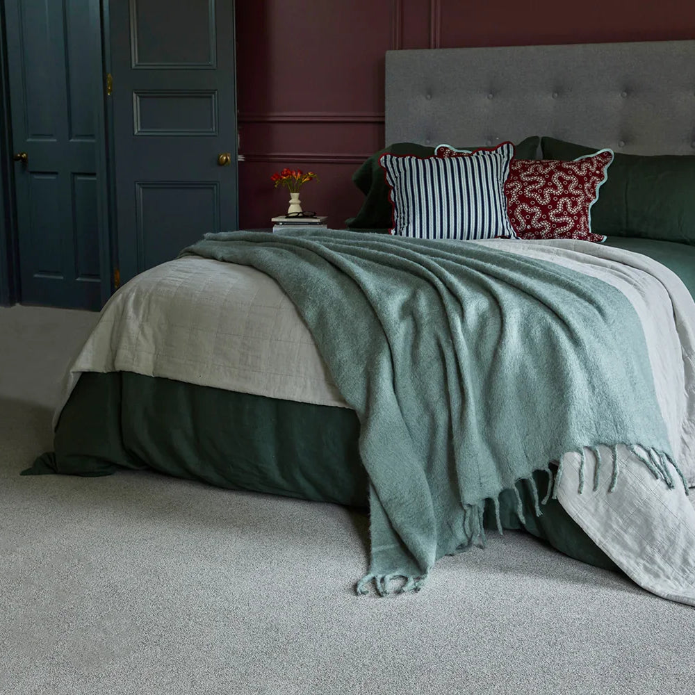 Modern bedroom with upholstered bed, layered bedding, scatter cushions, and grey carpet