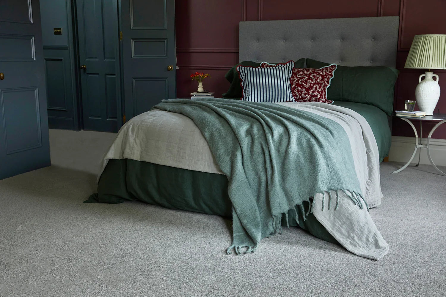 Modern bedroom with upholstered bed, layered bedding, scatter cushions, and grey carpet