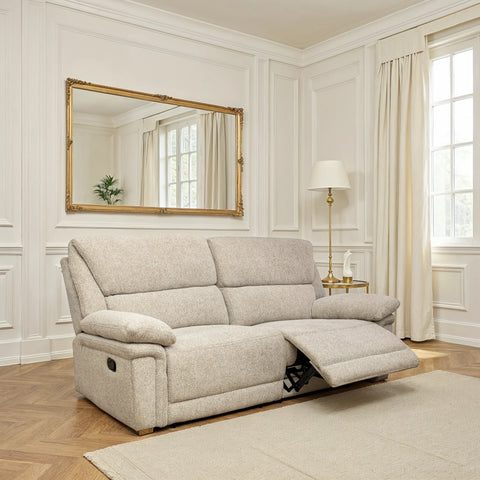 A light beige upholstered reclining loveseat sofa shown in a bright, white-paneled living room with a floor lamp, curtains, and a large gold-framed mirror.