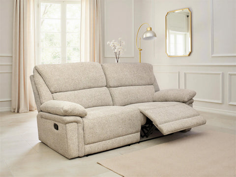 A light beige upholstered recliner sofa shown in a bright, modern living room with cream walls, curtains, a floor lamp, and a mirror. The sofa is shown in the reclined position with the footrest extended.